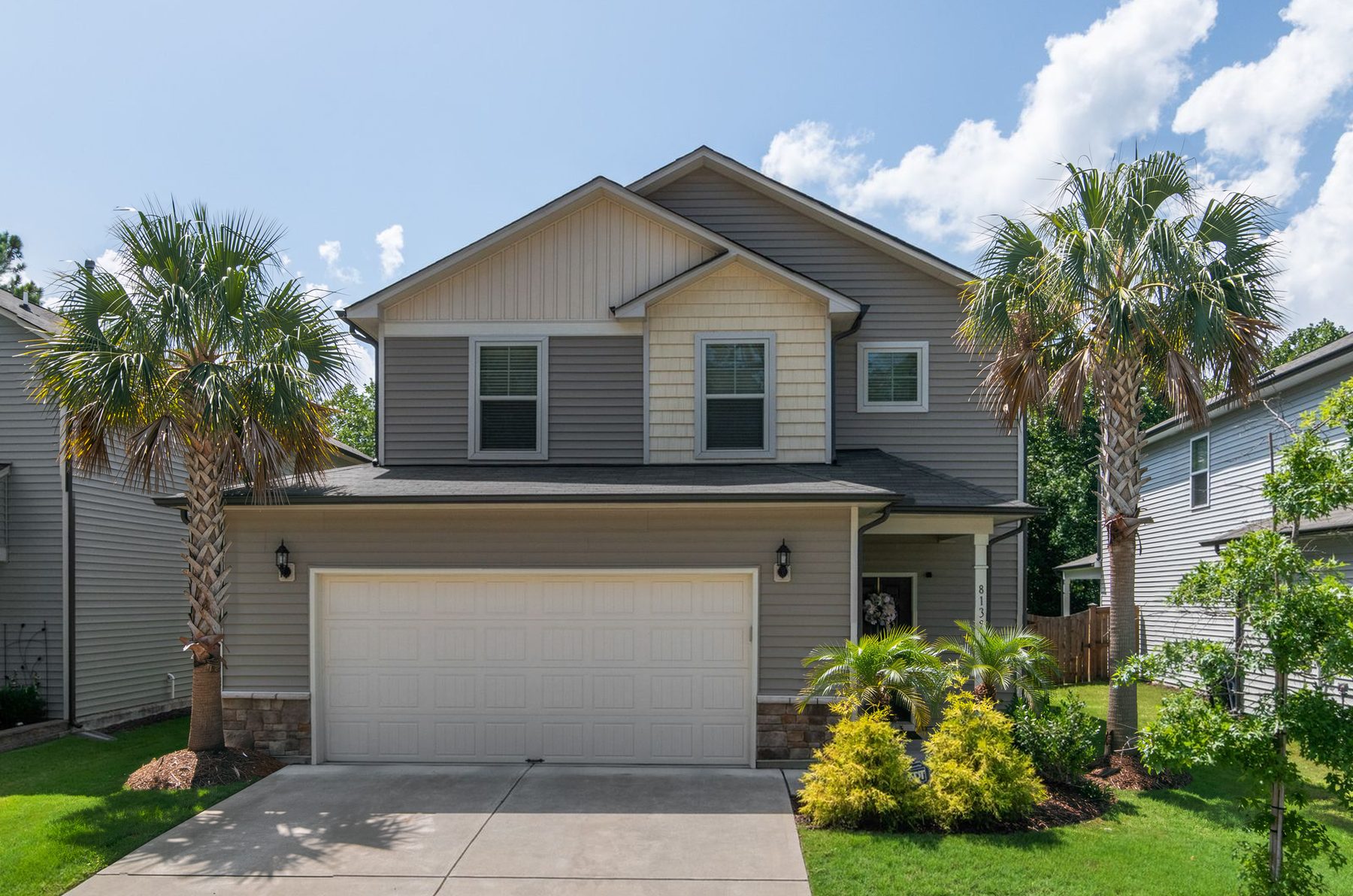 A two-story gray home with palm trees, a white two-car garage and a driveway